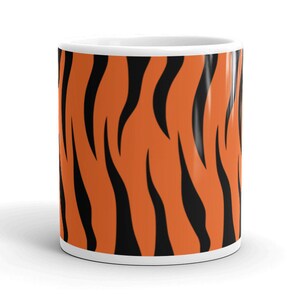 Puede incluir: Una taza de cerámica blanca con un patrón de rayas de tigre en naranja y negro.
