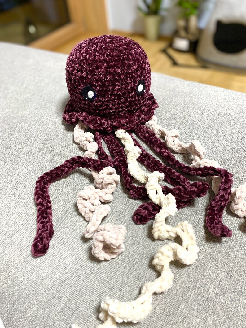 May include: A crocheted plush jellyfish toy with a burgundy body and white and pink tentacles. The jellyfish has black eyes.