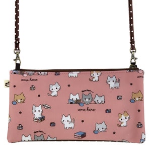 May include: A pink zippered pouch with a brown adjustable strap. The pouch has a repeating pattern of white, gray, and orange cats with the text "uma hara" printed on the pouch.