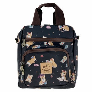 Puede incluir: Un bolso negro de bandolera con asa y correa marrones. El bolso está cubierto con un patrón de perros corgi, caballos de balancín y otras ilustraciones caprichosas. El bolso tiene varios bolsillos y cremalleras.