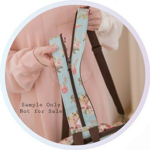 May include: A light blue tote bag with a floral print and brown straps. The bag has a zipper closure and the text "Sample Only Not for Sale" is printed on the front.