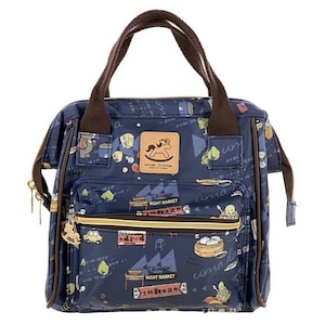 May include: Navy blue tote bag with a repeating pattern of illustrations and text. The bag has brown handles and a zipper closure. The front pocket has a zipper and a charm. The text "Taiwan Night Market" is visible.