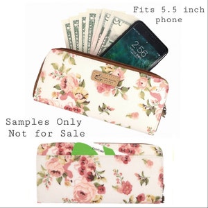 May include: A white zippered wallet with a floral print and a brown leather zipper pull. The wallet has a pocket for a 5.5 inch phone and a card slot. The text "Samples Only Not for Sale" is printed on the image.