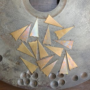 May include: A collection of 16 brass triangle-shaped pendants with a hammered finish. The pendants have three holes each, suggesting they are intended for jewelry making.