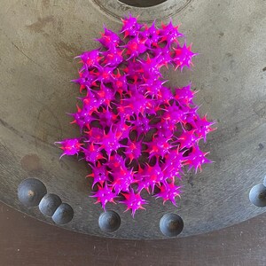 May include: A large pile of bright pink and neon pink star-shaped rubber toys on a gray metal surface.