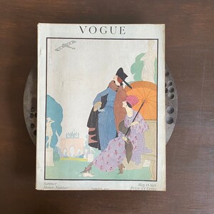 May include: A vintage May 15, 1918, issue of Vogue magazine, Summer Homes Number, priced at 25 cents. The cover features an illustration of two figures in period clothing, an orange parasol, a biplane, and an archway in a garden setting.