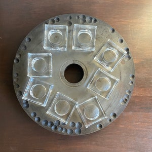 Può includere: Un vassoio rotondo in legno grigio con un foro centrale circolare e otto contenitori quadrati trasparenti attorno al bordo.
