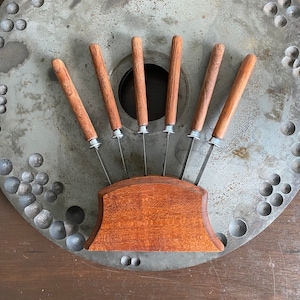 May include: A set of six wooden handled knives with silver blades are displayed in a wooden knife holder. The holder is a dark brown color and has a curved shape. The knives are arranged in a fan shape.