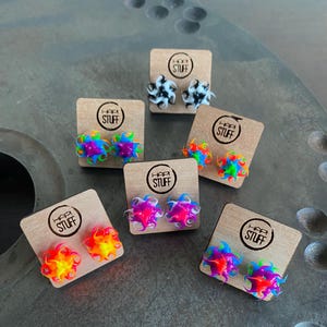 Könnte beinhalten: Sechs Paare farbenfroher, sternförmiger Ohrringe auf kleinen Holzkarten mit dem aufgedruckten Text "Happy Stuff".