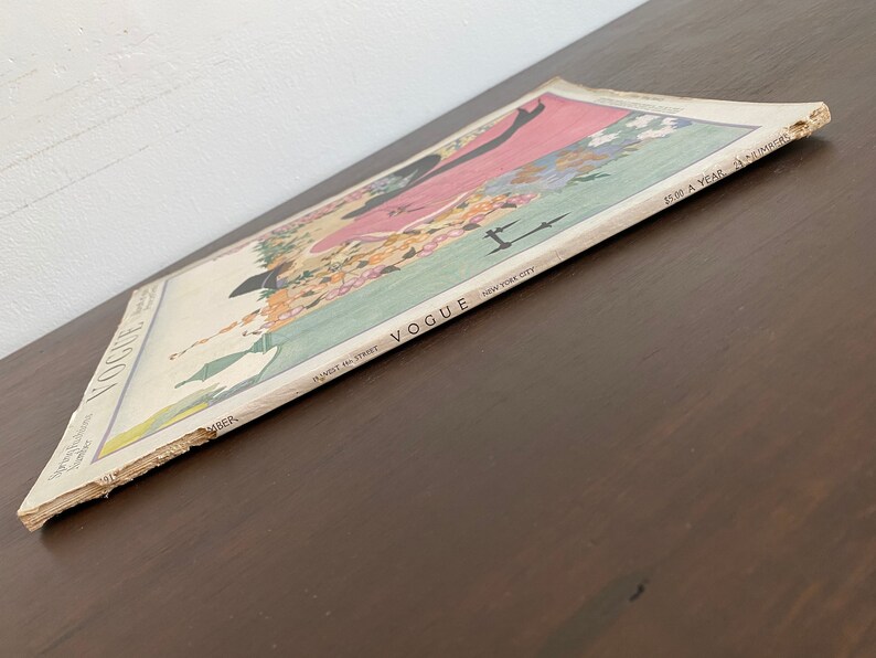 May include: A vintage Vogue magazine cover from November 1918, featuring a woman in a pink dress and a black hat. The cover is illustrated with flowers and the text "Vogue, 461 West 42nd Street, New York City, $5.00 a year, 24 numbers".