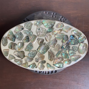 May include: Oval-shaped tray made of white resin with a mosaic of iridescent green, blue, and brown abalone shell pieces.
