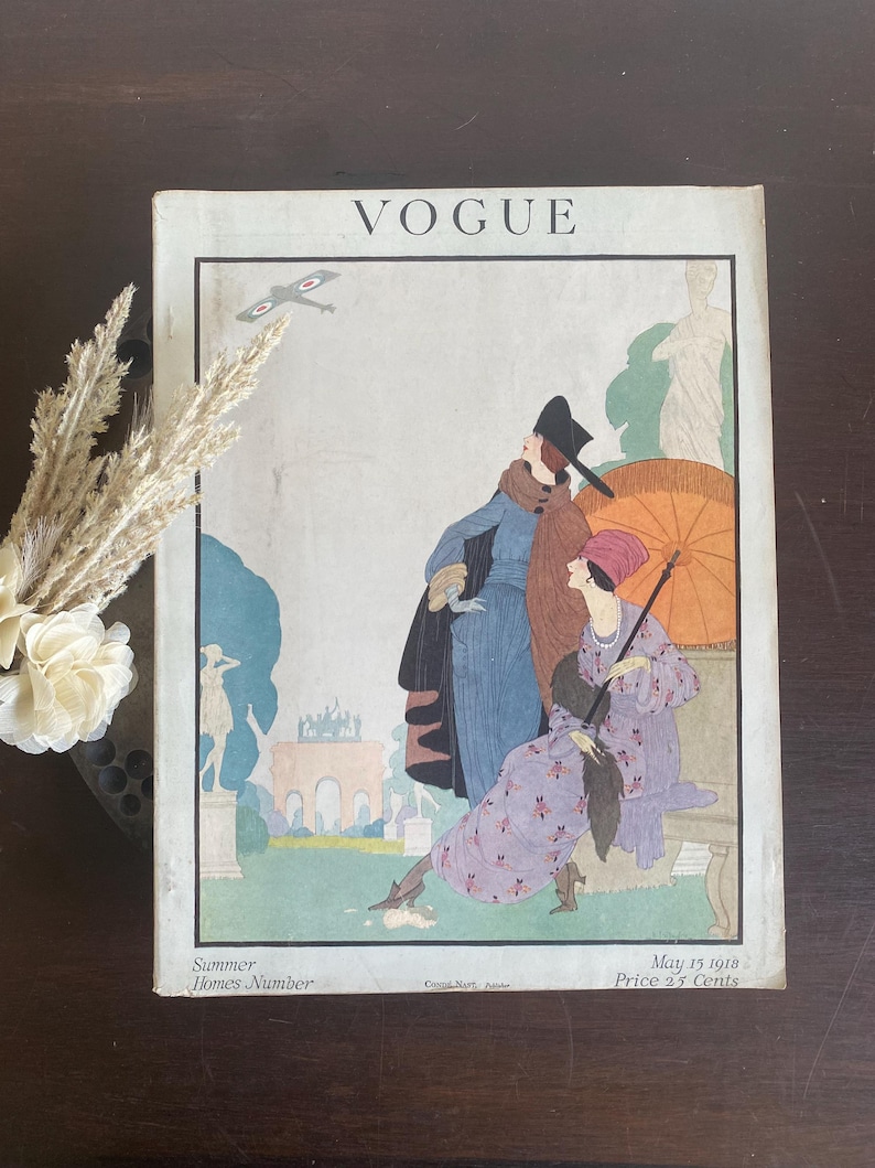 May include: A vintage Vogue magazine cover from May 15, 1918, titled Summer Homes Number. The illustration features two figures in period clothing, one holding an orange parasol, with a biplane in the sky and classical statues in a garden.