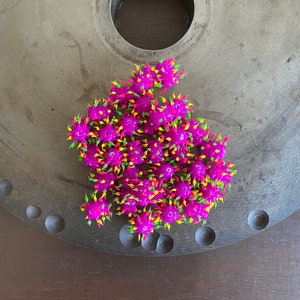 May include: A group of small, spiky, purple rubber balls with yellow and green accents. The balls are arranged in a cluster on a gray metal surface.