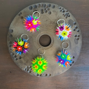 May include: Five colorful spiky keychain balls with silver key rings. The balls are made of rubber and have a variety of colors, including red, orange, yellow, green, blue, purple, and black.