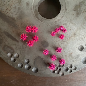 Può includere: Una collezione di palline di gomma rosa e viola con punte su una superficie di metallo grigia. Le palline sono disposte in un gruppo e alcune sono sparse sulla superficie.