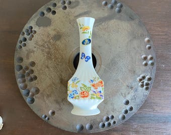Puede incluir: Un jarrón de porcelana blanca con un diseño floral y de mariposas. El jarrón tiene un cuello estrecho y una base ancha. Las flores son en tonos de rosa, amarillo y azul. Las mariposas son azules y blancas.