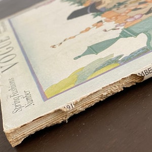 May include: A vintage Vogue magazine cover from 1917, featuring a colorful illustration of a woman in a garden setting. The cover text reads "Spring Fashions Number".