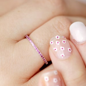 Peut inclure: Une délicate bague éternelle avec une fine bande de métal blanc sertie de minuscules pierres précieuses roses.