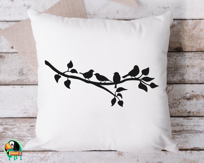 May include: A white throw pillow with a black silhouette of a branch with four birds perched on it. The branch has leaves and the birds are facing different directions.