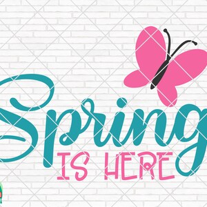 以下が含まれることがあります： ターコイズブルーの筆記体フォントで「Spring is Here」と書かれており、その上にピンクのバタフライが描かれています。背景は白いレンガの壁です。