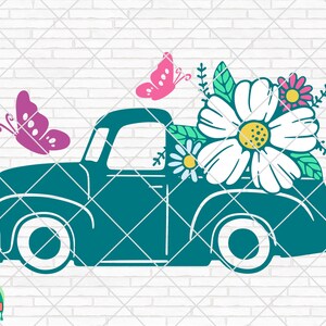 以下が含まれることがあります： 白い車輪が付いたターコイズブルーのヴィンテージピックアップトラックが、ピンクとグリーンのアクセントが付いた白いデイジーの花束を運んでいます。2匹のピンクの蝶がトラックの上を飛んでいます。