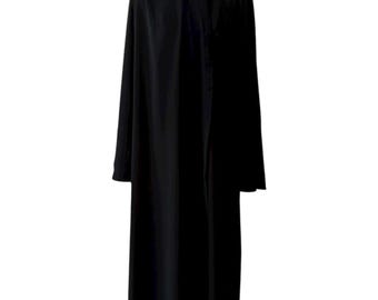 May include: A long, black dress with long sleeves and a high neckline. The dress is buttoned down the front and hangs to the floor. The garment is displayed on a black mannequin.