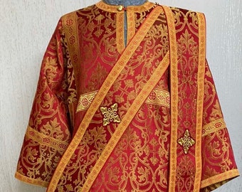 May include: A red and gold liturgical vestment with intricate floral patterns and gold trim. The vestment has a long, flowing design and features a decorative cross on the front.