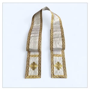 Könnte beinhalten: Eine cremefarbene liturgische Stola mit goldfarbenen Stickereien. Die Stola hat ein Holzmaserungsmuster und goldfarbene Verzierungen an den Rändern. Die Enden der Stola haben ein goldgesticktes Kreuzdesign.