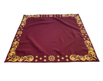 Puede incluir: Un mantel de altar de color burdeos con un borde bordado en oro que presenta intrincados diseños florales y motivos de cruces.