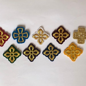 Könnte beinhalten: Sortiment von zehn gestickten Aufnähern mit Goldfaden-Designs auf verschiedenen Filz-Hintergründen. Die Designs umfassen Kreuze und Kleeblätter.