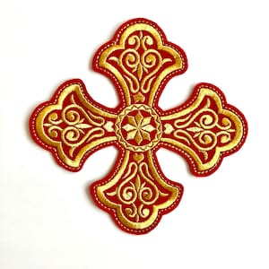 Puede incluir: Una cruz roja bordada con detalles en hilo dorado. La cruz tiene un diseño tradicional con intrincados patrones florales.