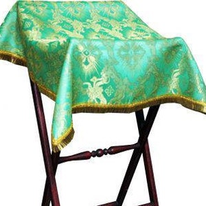 May include: Green altar cloth with a gold floral pattern and gold fringe. The cloth is draped over a wooden altar stand.
