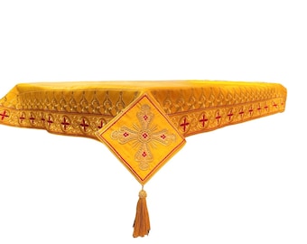 Puede incluir: Un mantel de altar dorado con un borde bordado en rojo y dorado y una cruz dorada con un borla.
