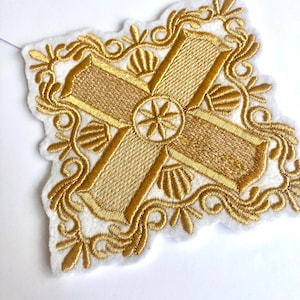 Peut inclure: Une croix brodée dorée avec une bordure florale décorative. La croix est sur un fond blanc.