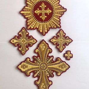 Könnte beinhalten: Ein Set aus sechs gestickten Aufnähern mit goldenen Kreuzen auf rotem Hintergrund. Der größte Aufnäher ist ein Stern mit einem Kreuz in der Mitte. Die anderen Aufnäher sind Kreuze in verschiedenen Größen und Formen.