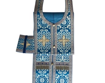 Puede incluir: Una vestimenta litúrgica azul con bordados dorados y una estola a juego. La vestimenta tiene un diseño tradicional con una cruz y motivos florales.
