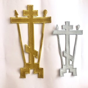 Könnte beinhalten: Zwei gestickte Patches mit einem Kreuz und einem Speer auf jeder Seite. Der größere Patch ist golden und der kleinere ist silbern.