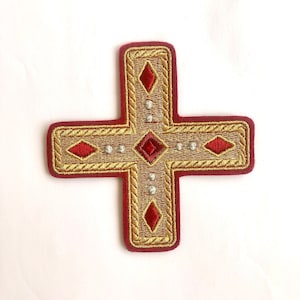 May include: A red cross with gold embroidery and a diamond pattern. The cross is decorated with small, white beads.