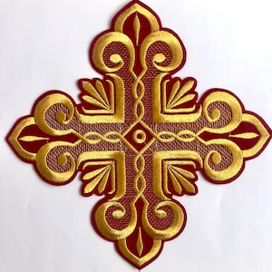 May include: A red embroidered cross with gold thread detailing. The cross has a traditional design with intricate swirls and flourishes.
