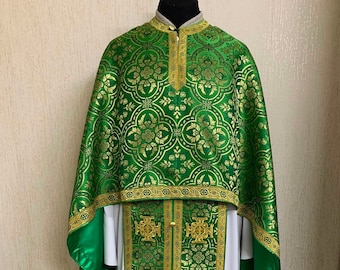 May include: Green and gold liturgical vestments. The vestments feature an ornate floral pattern in gold on a green background. The trim is gold with decorative detailing. The undergarment is white. The vestments are displayed on a mannequin.