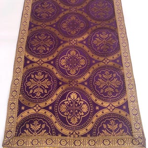 May include: Purple and gold fabric runner with a repeating pattern of circles and floral designs. The runner has a gold fringe border.