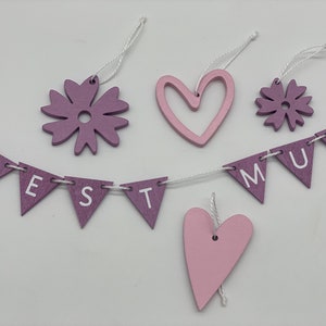 Op de afbeelding: Een paarse en roze houten banner met de woorden "BEST MUM" geregen aan een wit touwtje. De banner is versierd met twee paarse bloemen en twee roze harten.