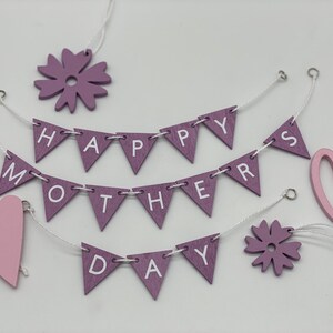 Op de afbeelding: Paarse en roze houten decoraties met de woorden "Happy Mothers Day" op een banner. De decoraties omvatten harten, bloemen en een banner.