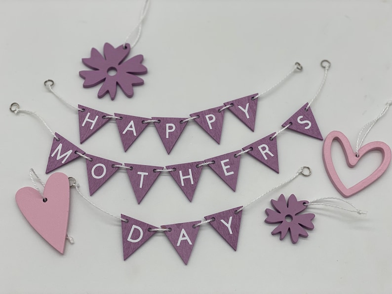 Op de afbeelding: Paarse en roze houten decoraties met de woorden "Happy Mothers Day" op een banner. De decoraties omvatten harten, bloemen en een banner.