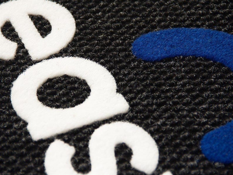 Puede incluir: Primer plano de una alfombra de bienvenida negra con la palabra "SAFE" en letras blancas en relieve y una forma curva azul.