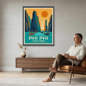 May include: A framed travel poster featuring a stylised illustration of Phi Phi, Thailand. The artwork depicts tall dark blue cliffs, turquoise water, and traditional long-tail boats under a large orange sun. The text reads PHI PHI THAILAND ISLANDS OF ADVENTURE.