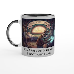 Könnte beinhalten: Eine weiße Keramik-Tasse mit schwarzem Innenraum und Henkel. Die Tasse zeigt eine farbenfrohe Illustration einer Person in einem Raum mit dem Text "I DON'T RISE AND SHINE - I BOOT AND LOAD".