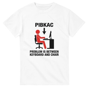 May include: White t-shirt with a humorous graphic. The design features a red stick figure seated at a desk with a computer, and the text "PIBKAC" above an arrow pointing down, and the phrase "PROBLEM IS BETWEEN KEYBOARD AND CHAIR" below.