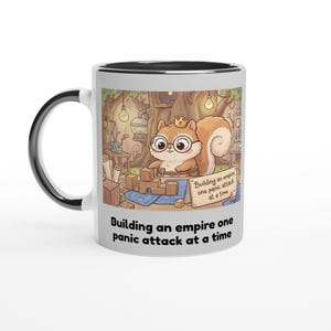 Peut inclure: Mug en céramique blanche avec intérieur et anse noirs. Il présente un écureuil de dessin animé avec des lunettes et une couronne, construisant avec des blocs. Le texte sur la tasse dit "Building an empire one panic attack at a time."
