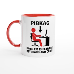 Könnte beinhalten: Weißer Keramikbecher mit rotem Innenraum und Henkel. Der Becher zeigt den Text "PIBKAC" über einer Grafik einer Person am Computer mit den Worten "PROBLEM IS BETWEEN KEYBOARD AND CHAIR" darunter.